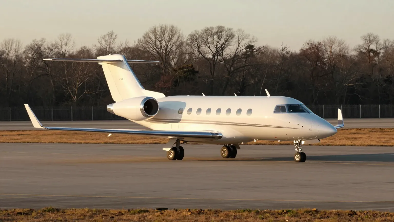 A white midsize business jet parked alone on an empty regional airport ramp at golden hour in late autumn.