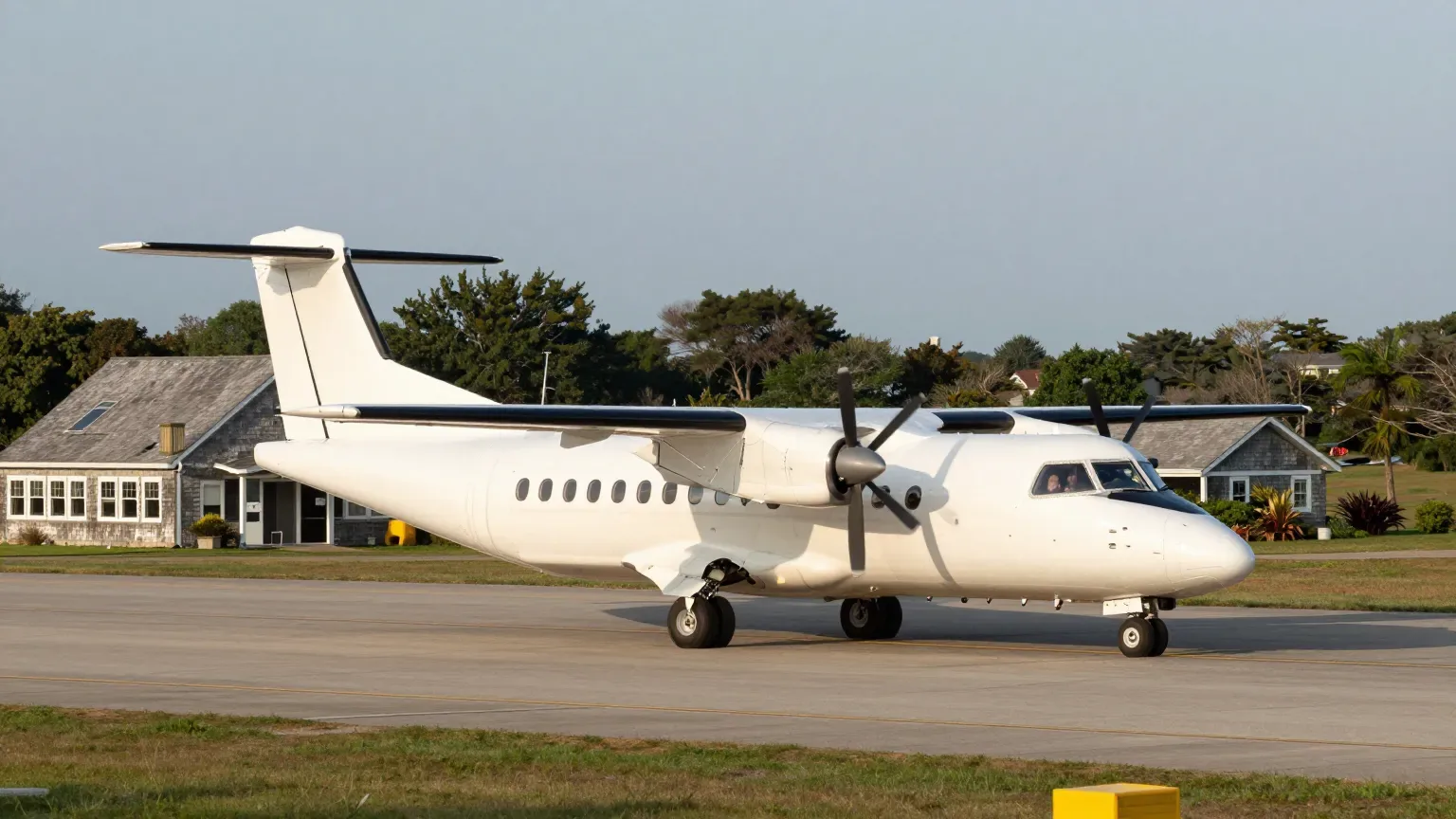 A turboprop on the ramp at Martha's Vineyard Airport, the island's grey-shingle terminal behind it in late-summer light.